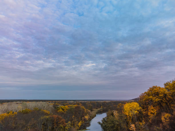 Autumn landscape, river and yellow trees forest with scenic blue cloudy sky. Aerial riverside in Ukraine