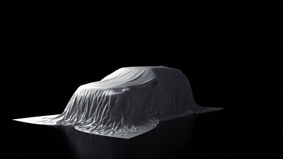 The front view of a big car, headlights aglow, shrouded in white fabric against a black background.