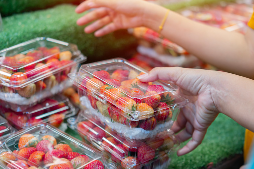Fresh red strawberries in woman hand arranged in baskets ready for sale at marketplace. Selective focus.