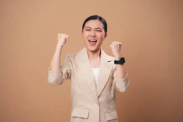 Photo of Asian woman happy confident make a winning gesture standing isolated on beige background.