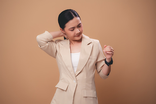Asian woman feels pain suffering from injury neck ache standing isolated on beige background.