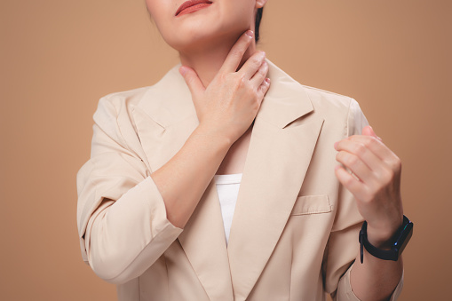 Close-up shot of woman was sick with fever having sore throat inflammation tonsils standing isolated on beige background.