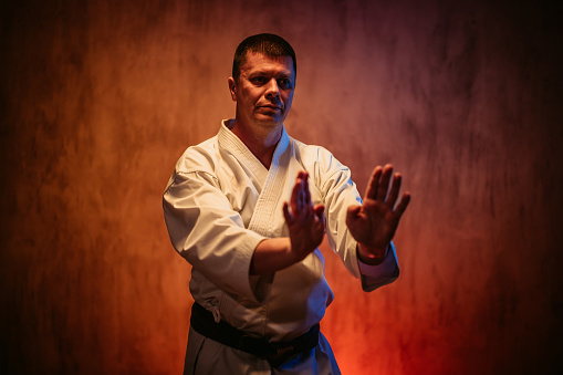 Mid-adult man wearing a white kimono practicing karate against red grunge background.