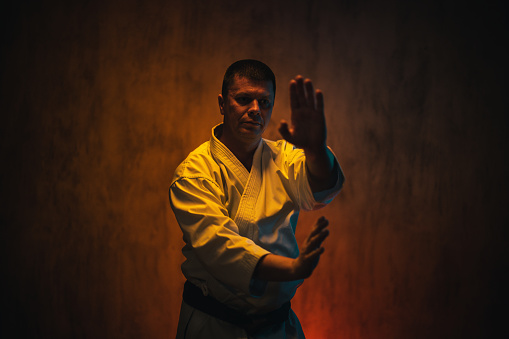 Mid-adult man wearing a white kimono practicing karate against dark grunge background.