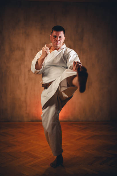 istock Mid-Adult Man Wearing A White Kimono Practicing Karate Against Dark Grunge Wall 1999689242