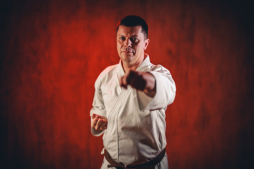Portrait of a mid-adult man wearing a white kimono practicing karate against red grunge background.