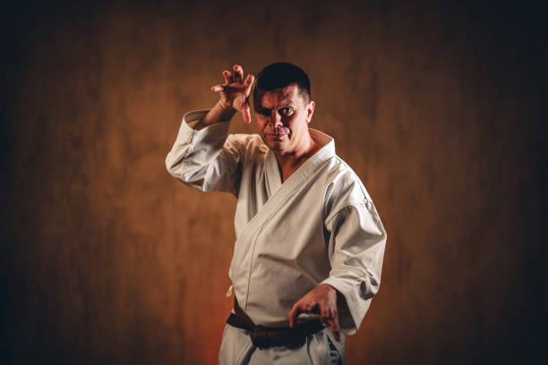 Portrait of a mid-adult man wearing a white kimono practicing karate against dark grunge background.