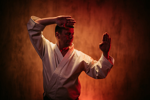 Mid-adult man wearing a white kimono practicing karate against red grunge background.