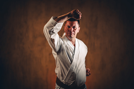 Portrait of a mid-adult man wearing a white kimono practicing karate against dark grunge background.