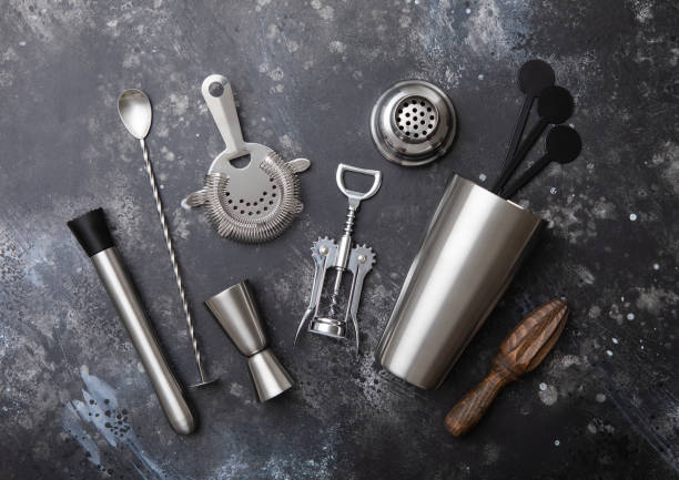 istock Steel various cocktail shaker,strainer,jigger and plastic stirrers with muddler on black background with manual wooden juicer and wine corkscrew. 1999699724