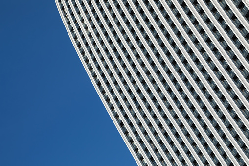 A minimalistic photo of a part of a modern building with repetitive pattern on its exterior stands out against the clear blue sky.