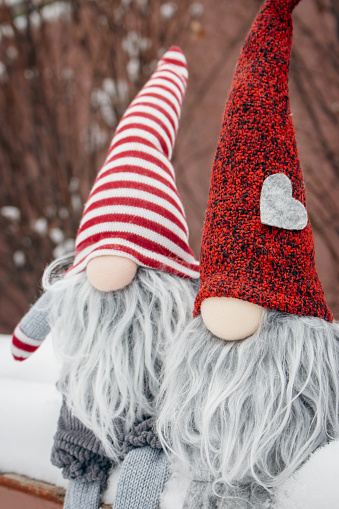 Couple of dwarves on the bench in snow. Romantic gift. Friendship concept. Valentine's Day concept. Gnomes with heart and red hat in snow. Love background. Christmas fairytale dwarves. Winter holidays decoration.