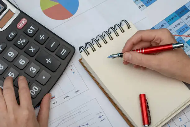 Photo of A man writes down financial data from tables and charts in a notebook