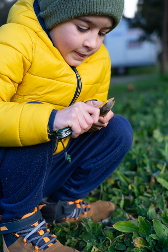 Boy peeling a forest stick with a pocket knife to make a spear