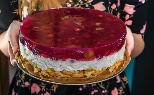 The girl holds in her hands a plate with a cake for the party, a cold cheesecake with jelly