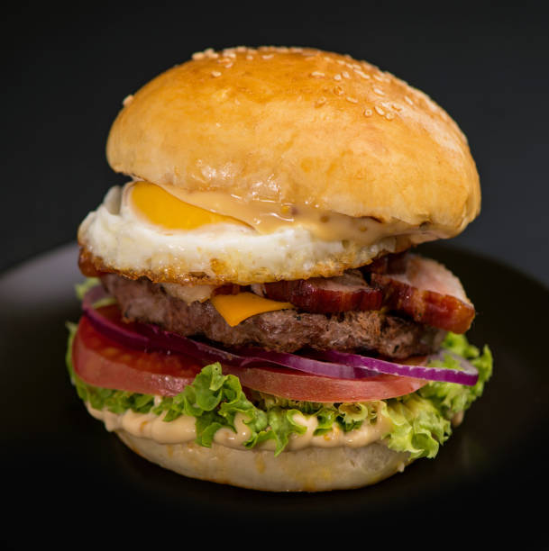 istock Big tasty burger with beef cutlet, lettuce, egg and cheese on a black background 1999753796