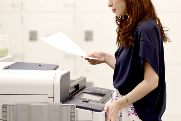 istock Young Asian female office worker checking documents in front of the office printer 1999808646