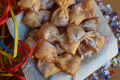 Italian sweet crisp pastry deep-fried in shape of a bow on a green plate on table. Chiacchere or crostoli, bugie, cenci with colorful paper confetti