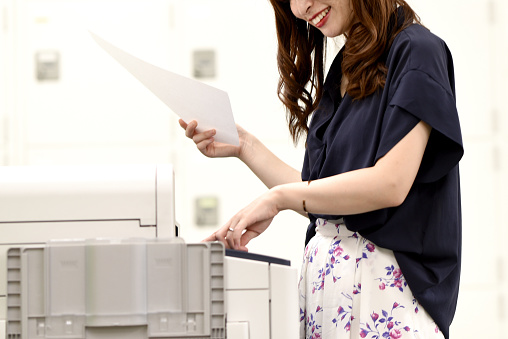 Young Asian female office worker checking documents in front of the office printer