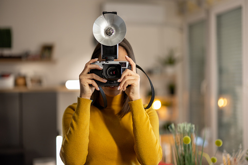 Beautiful young woman photographing on vintage camera at home