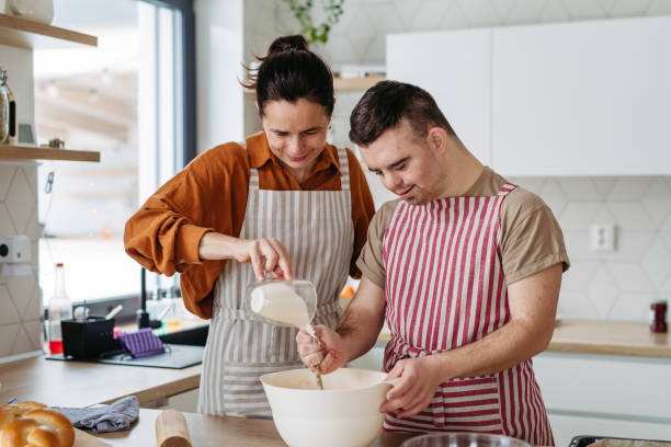 istock Young man with Down syndrome preparing breakfast with his mother at home, cracking eggs. Morning routine for man with Down syndrome. 1999843337