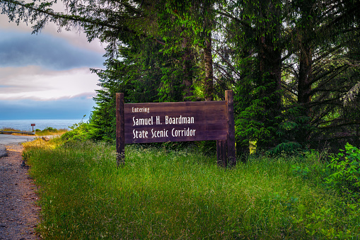 Road leading into Samuel H. Boardman State Scenic Corridor in Oregon with welcome sign and greenery.