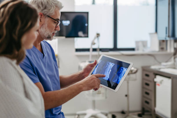 Doctor showing female patient MRI scan on tablet, discussing test result in emergency room. Doctor showing female patient MRI scan on tablet, discussing her test result in emergency room. melancholy computer support specialist stock pictures, royalty-free photos & images