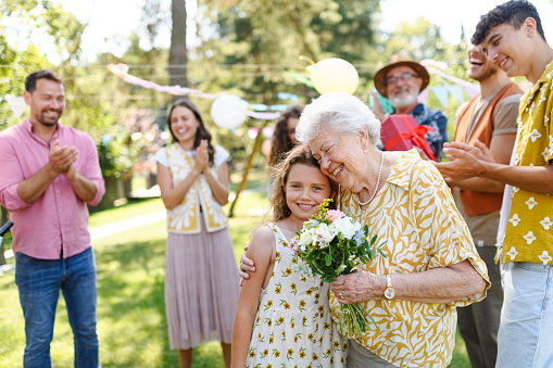 Garden birthday party for senior lady. Beautiful senior birthday woman receiving flowers from granddaughter.