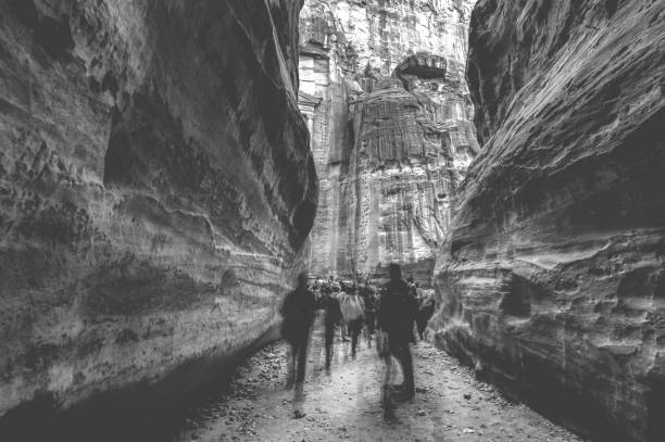 Group of people between sandstone rocks at narrow path in Petra, Jordan, black and white