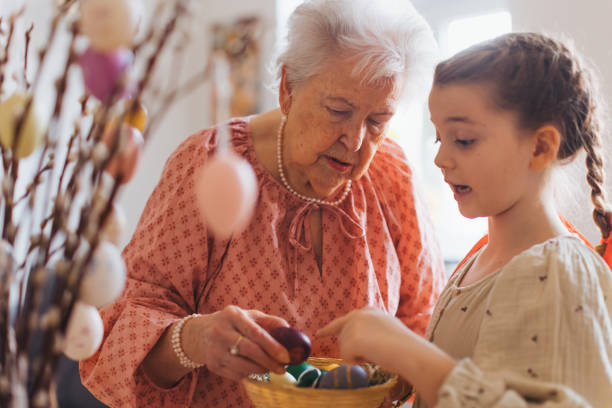 istock Grandmother with grandaughter decorating pussy willows branches, putting easter eggs on them. 1999896898