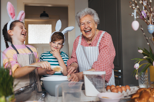 Grandmother with grandchildren preparing traditional easter meals, baking cakes and sweets. Passing down family recipes, custom and stories. Concept of family easter holidays.