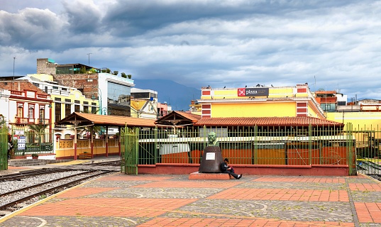 Riobamba, Ecuador, October 28, 2022: A man sits by the statue of Eloy Alfaro in the Plaza Eloy Alfaro under cloudy sky.