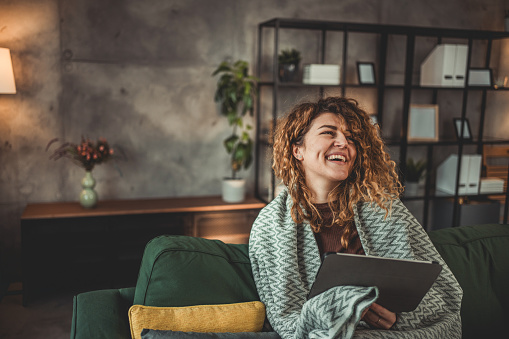 A young woman is watching an online movie on her tablet, sitting on an sofa in the living room