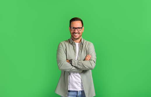 Portrait of young businessman with arms crossed smiling and posing over isolated green background