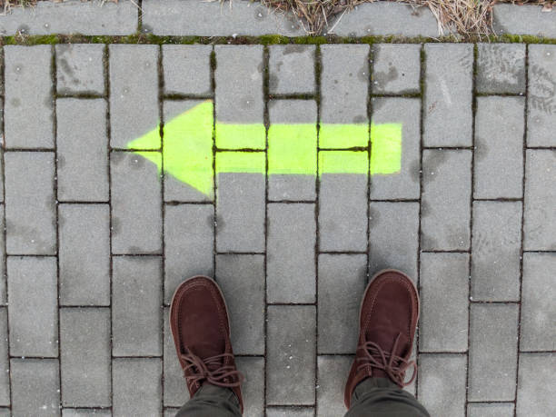 Feet in boots on a paving stone with a light green arrow painted on it.
