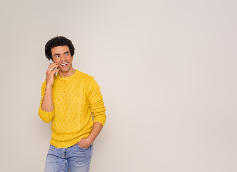Smiling young salesman with afro hair talking over smart phone and looking away on white background