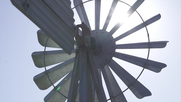 A traditional steel windmill on a farm, backlit by the bright afternoon sun, against a clear blue sky in the outback