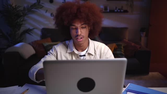 Front view of an overwhelm young African american male studying late from home using a laptop.