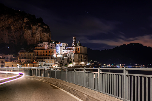 a passing car offers a trail of light along the road leading to the small village of Atrani on the Amalfi Coast