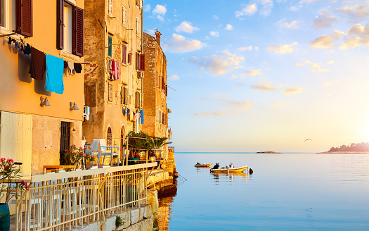 Rovinj, Istria, Croatia. Antique medieval houses at coastline of Rovigno, Adriatic Sea. Sunrise with blue sky and fishing boats on the water. Calm silent summer morning sea.