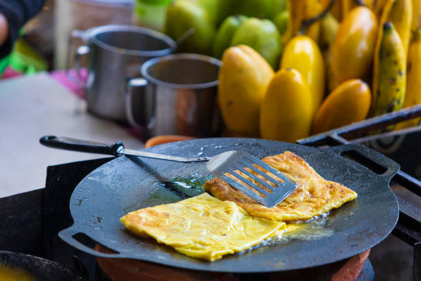 Pancakes Roti, Thailand. Frying of roti snack on black pan. Indian traditional street food in Thailand. Thai pancake with banana and egg. Sweet crispy Roti Canai. Selective focus, blurred background