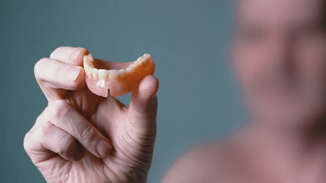 Elderly Male Holding a Denture of the Upper Jaw in Hands on a Blurred Background