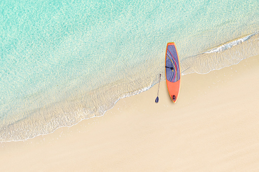 Top view of SUP board for surfing on the shore on tropical Seychelles sand beach. Blue, turquoise transparent water surface of ocean, sea, lagoon. Aerial, drone view