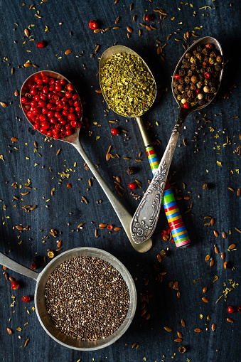 Old metal spoons with different herbs and spices on black background. Flat lay. Top view. Food concept. Dark mood food photography.