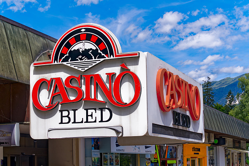 Close-up of red black and white sign at entrance of Casino of Slovenian City of Bled on a blue cloudy summer day. Photo taken August 8th, 2023, Bled, Slovenia.