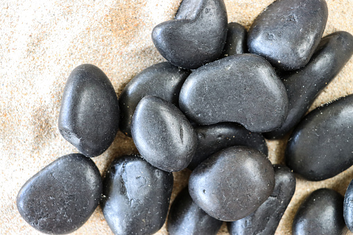 Stock photo showing close-up, elevated view of a pile of black stones on a sandy beach background.