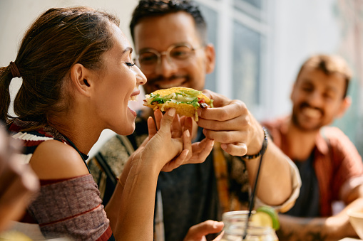Young woman eating her boyfriend's tacos during a lunch in Mexican restaurant.