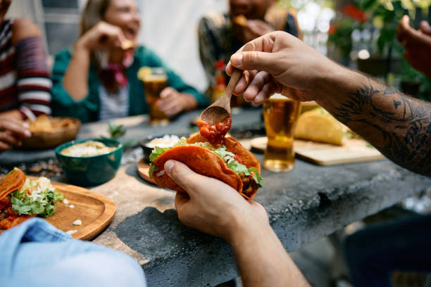 istock Close up of man adding salsa sauce while eating tacos in restaurant. 2000122761