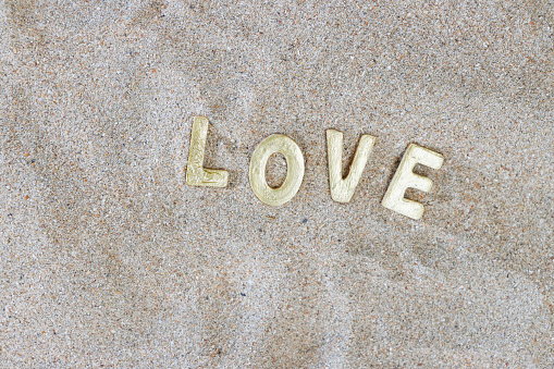 Stock photo showing close-up, elevated view of background of soft, dry golden beach sand with gold lettering spelling 'love'.