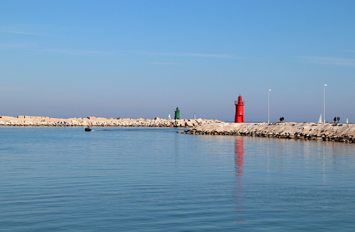 Trani, Province of Barletta-Andria-Trani, Italy - 04 february 2024: the San Nicola pier with the green lighthouse, and a pleasure boat return to port.